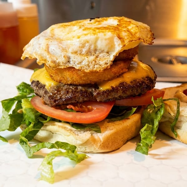 A gourmet burger with a fried egg, onion rings, cheese, patty, tomato, and lettuce.